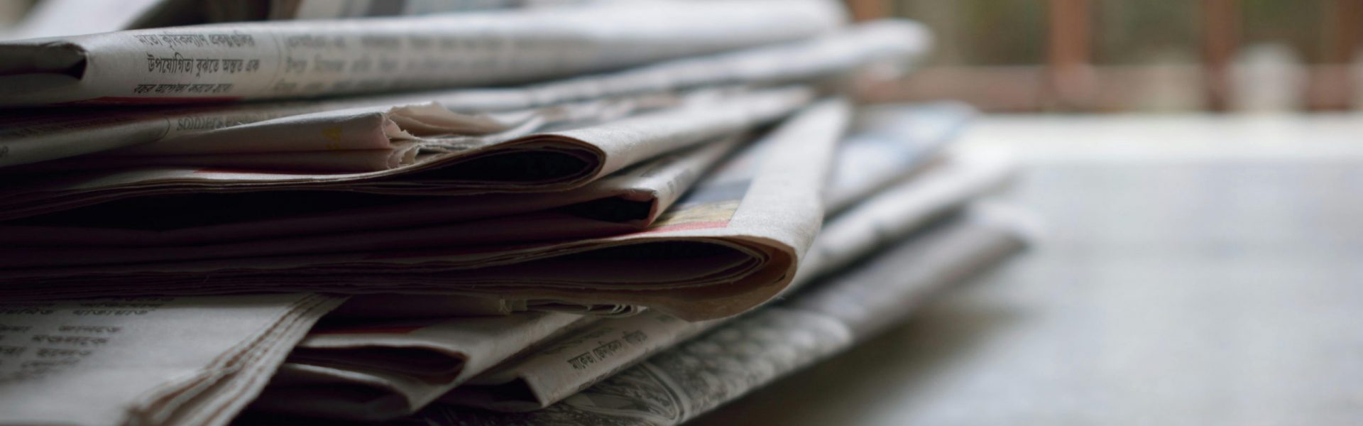 A close-up of a stack of newspapers resting on a desk, symbolizing information and media.